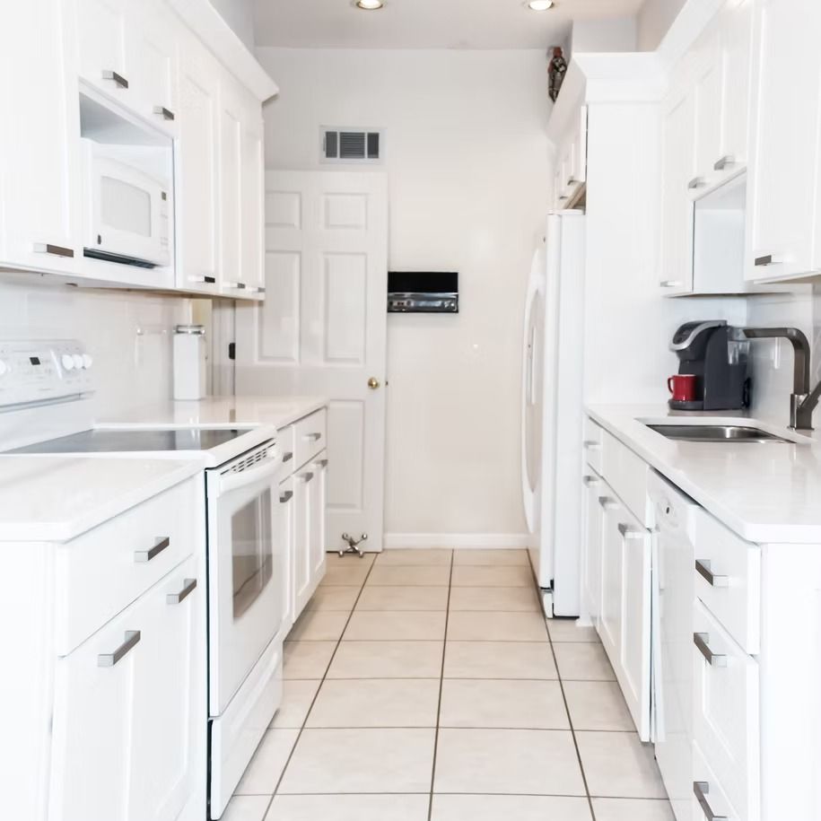 Bright white galley kitchen with white cabinets, tiled floor, and black countertop appliances