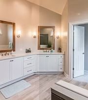 Bright bathroom with white cabinets, double sinks, mirrors, and warm wall sconces