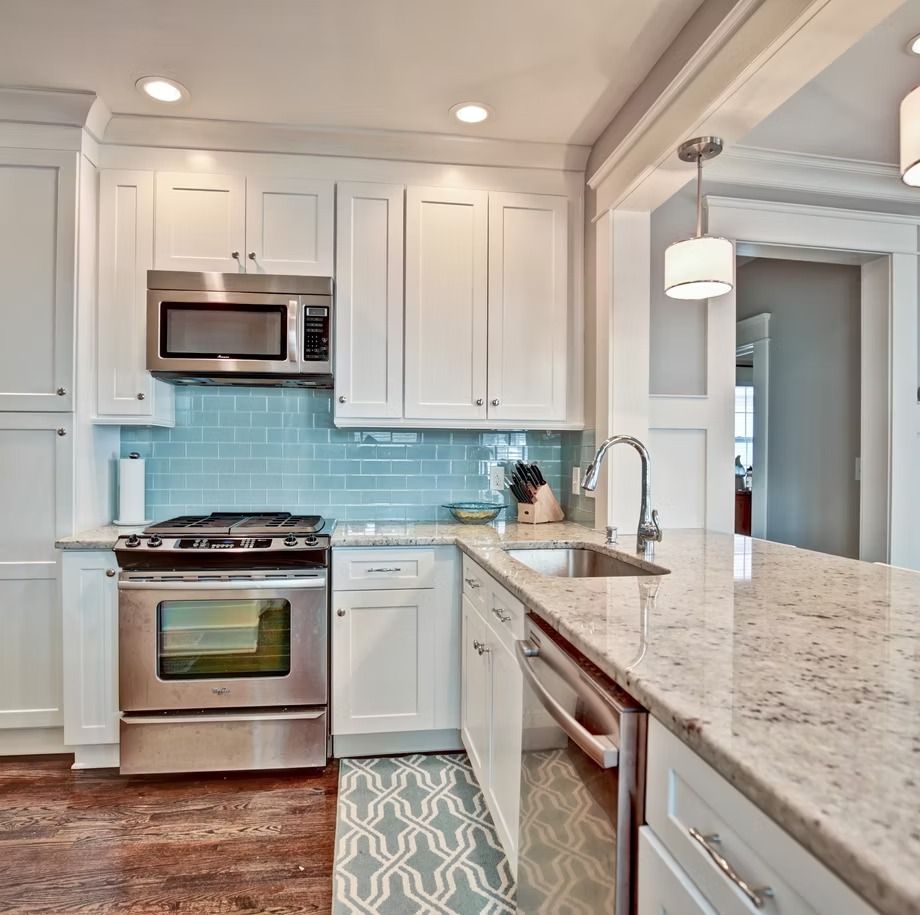Bright modern kitchen with white cabinets, stainless appliances, blue tile backsplash, and marble island counter