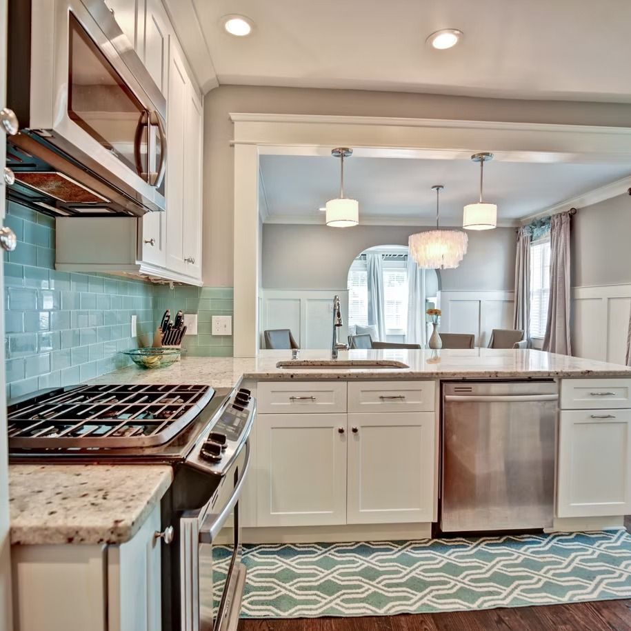 Bright kitchen with white cabinets, turquoise tile backsplash, stainless appliances, and a dining area beyond
