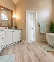 Bright beige bathroom with double vanity, mirror, towel rack, and bathtub near a white door.