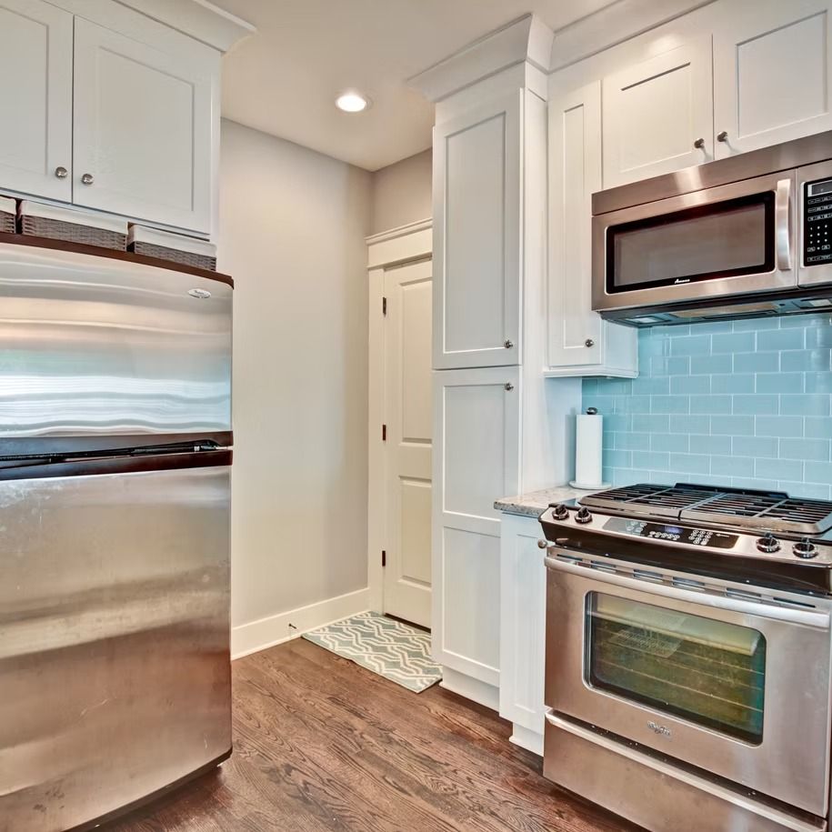 Bright modern kitchen with stainless steel appliances, white cabinets, and blue tile backsplash