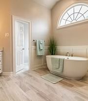 Bright beige bathroom with freestanding tub, window, towel rack, and light wood floor.