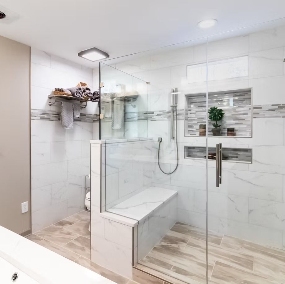 Modern glass shower with built-in bench in a bright, marble-tiled bathroom