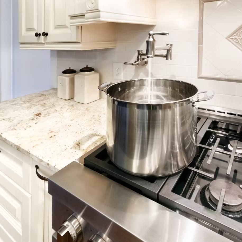 Large stainless steel pot on a gas stove with water pouring from a faucet in a bright white kitchen