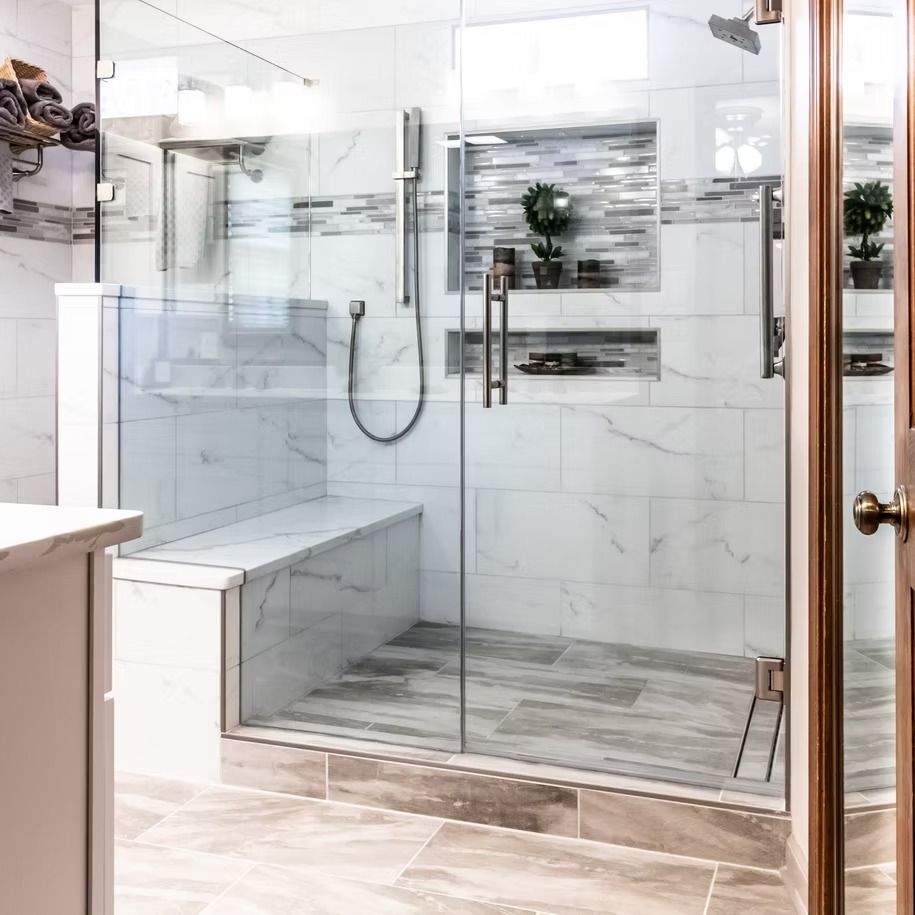 Modern glass walk-in shower with white marble tile, bench seat, and handheld showerhead