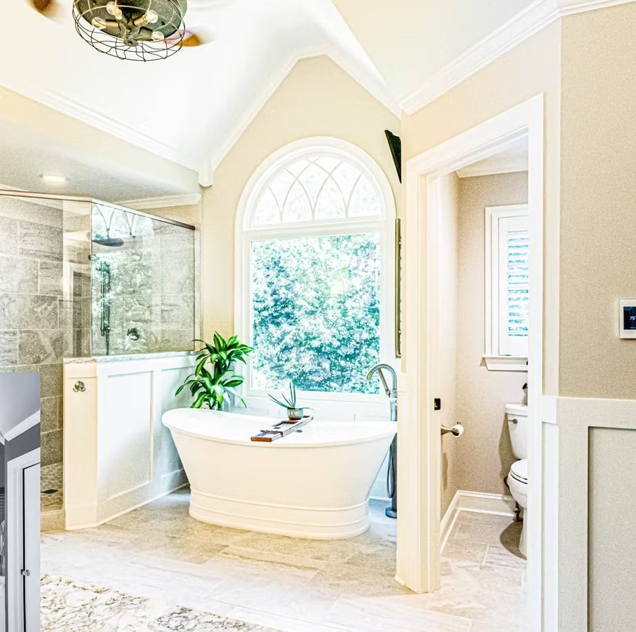 Bright spa-style bathroom with a freestanding tub, arched window, and glass shower.