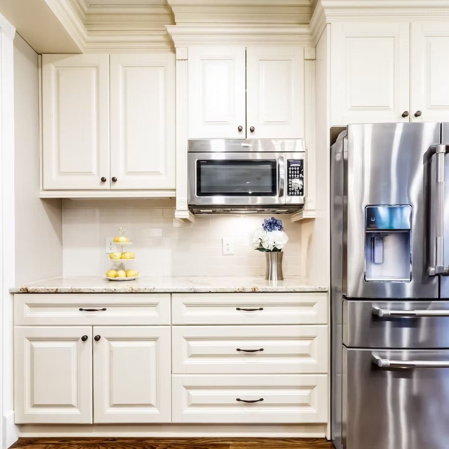 Bright white kitchen with cabinets, microwave, and stainless steel refrigerator on the right.