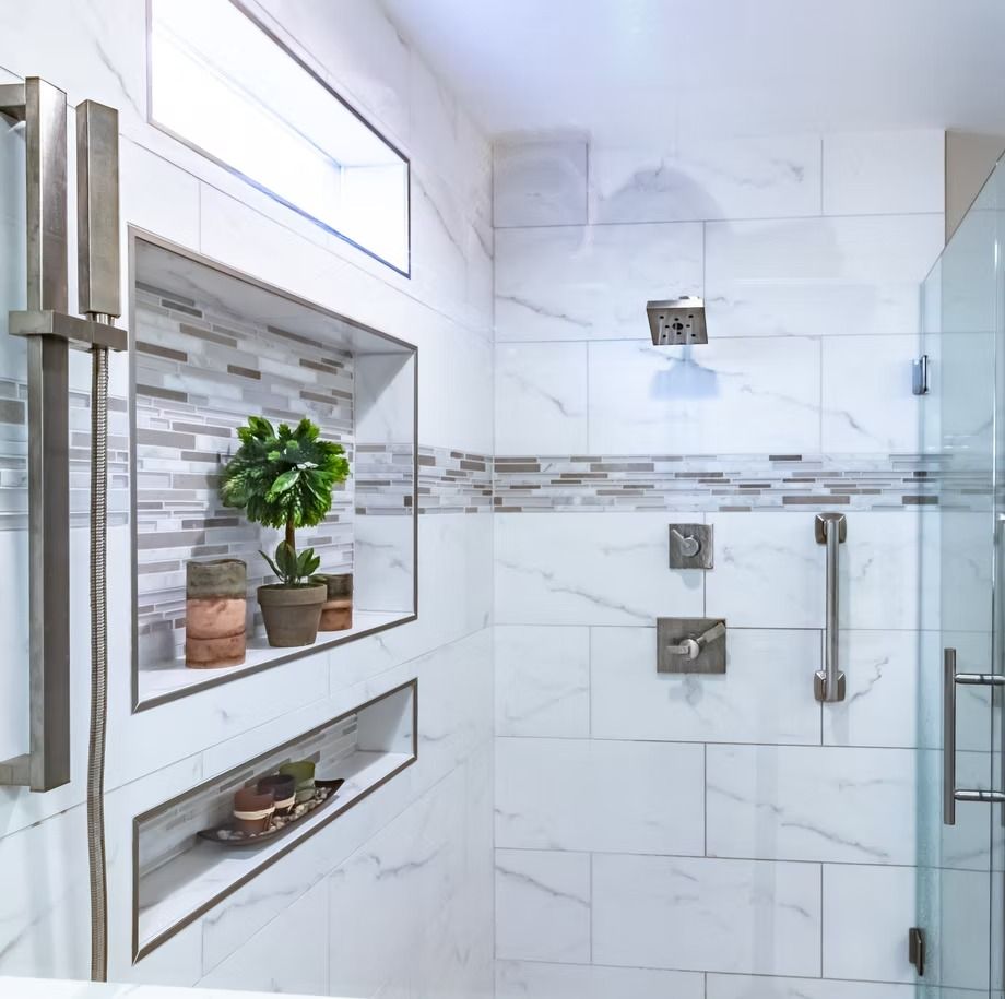 Modern white tiled walk-in shower with glass door, chrome fixtures, and a recessed shelf with potted plants
