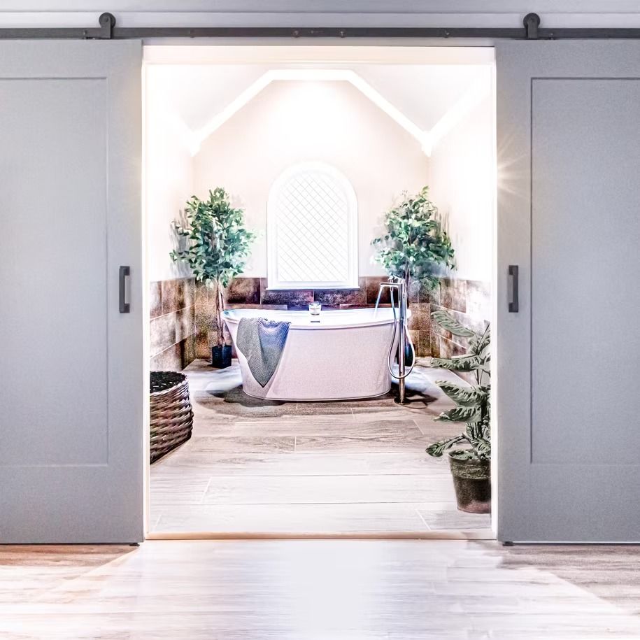 Open double doors to a bright room with a round table, draped linens, and lush greenery.