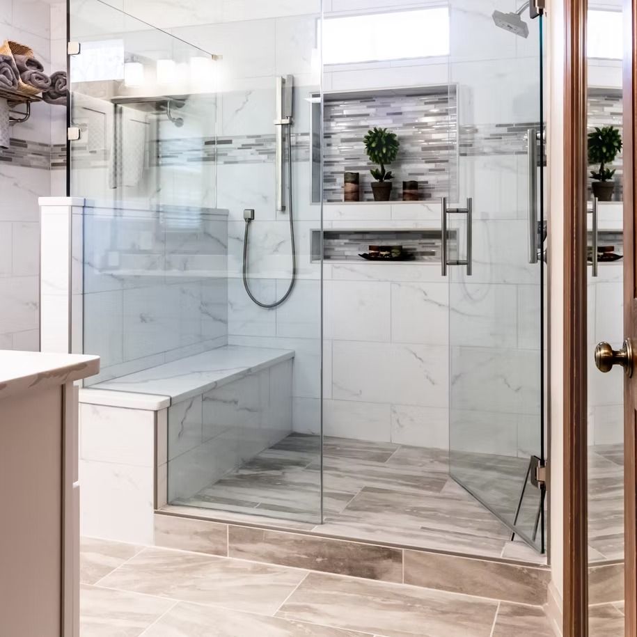 Modern bathroom with a glass walk-in shower, marble tile, built-in bench, and chrome fixtures
