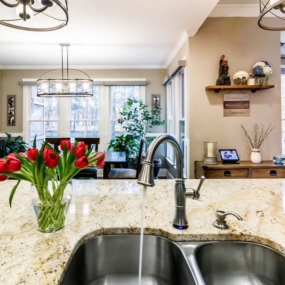 Kitchen with granite island, stainless sink, red tulips, and view into a bright dining and living area.