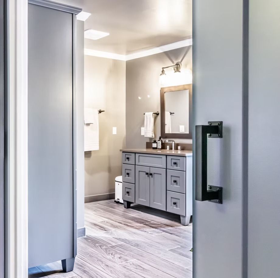 Bathroom doorway view with gray vanity, mirror, and wall sconce over light wood-look flooring