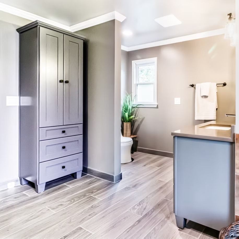 Bright gray bathroom with vanity, tall storage cabinet, window, and potted plant