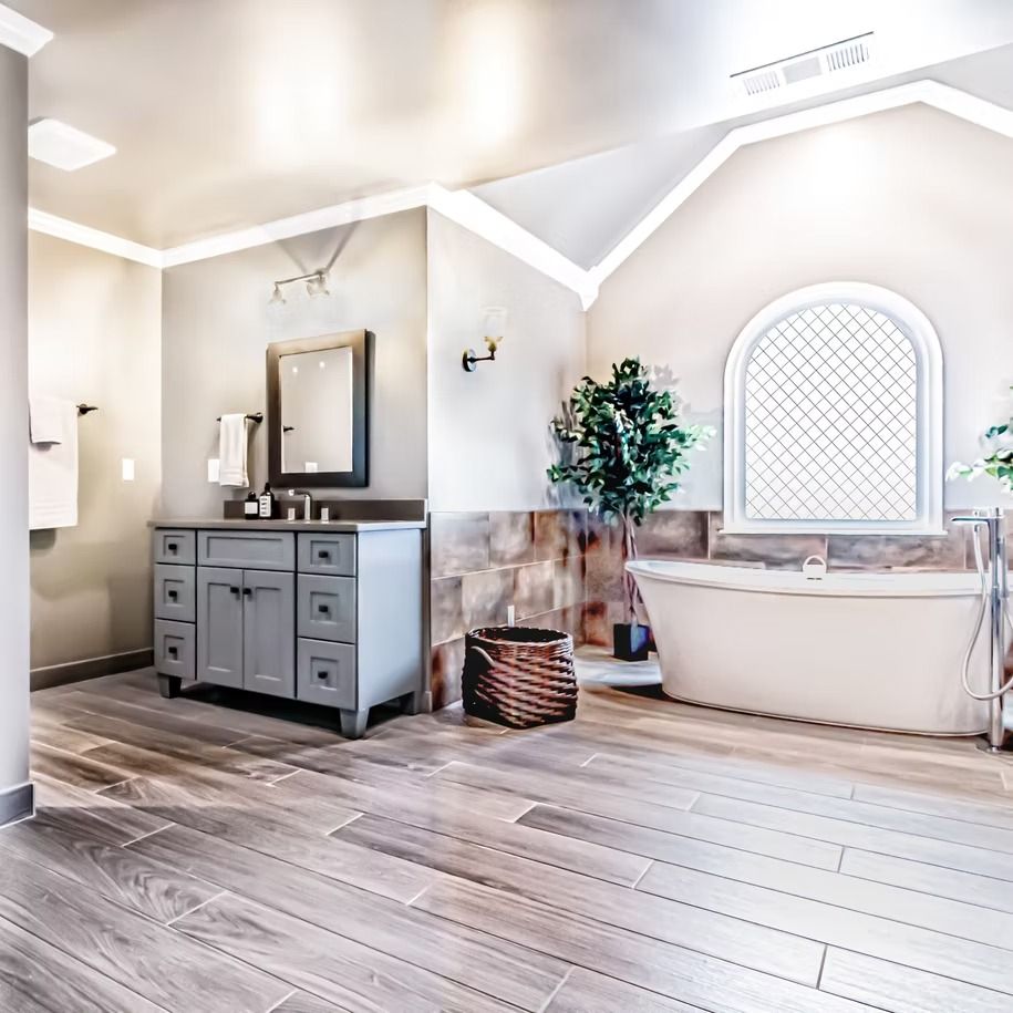 Bright modern bathroom with gray vanity, freestanding tub, arched window, and wood-look tile floor
