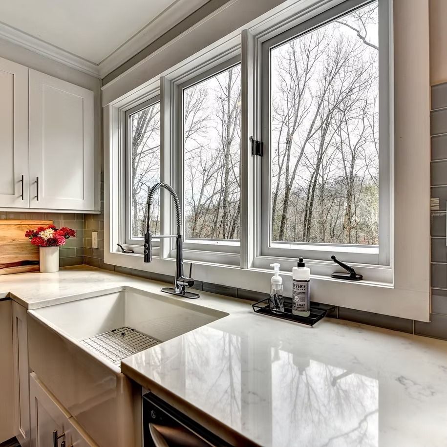 Bright kitchen with white cabinets, marble counters, sink, and large windows overlooking bare trees