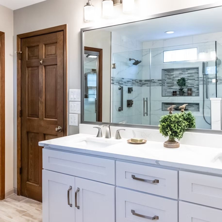 Modern bathroom vanity with double sinks, large mirror, and glass shower in the background