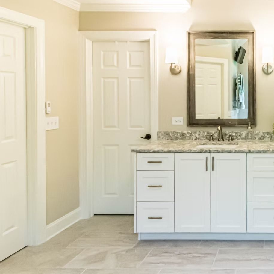 Bright beige bathroom with white vanity, granite countertop, large mirror, and two closed doors.