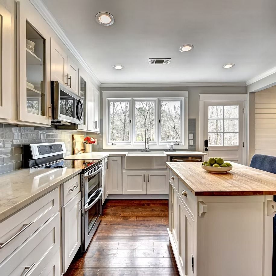 Bright modern kitchen with white cabinets, stainless appliances, wood island, and large window.