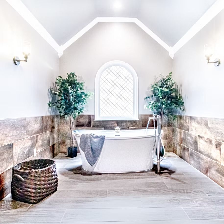 Bright spa bathroom with a freestanding tub, arched window, stone walls, plants, and wicker basket