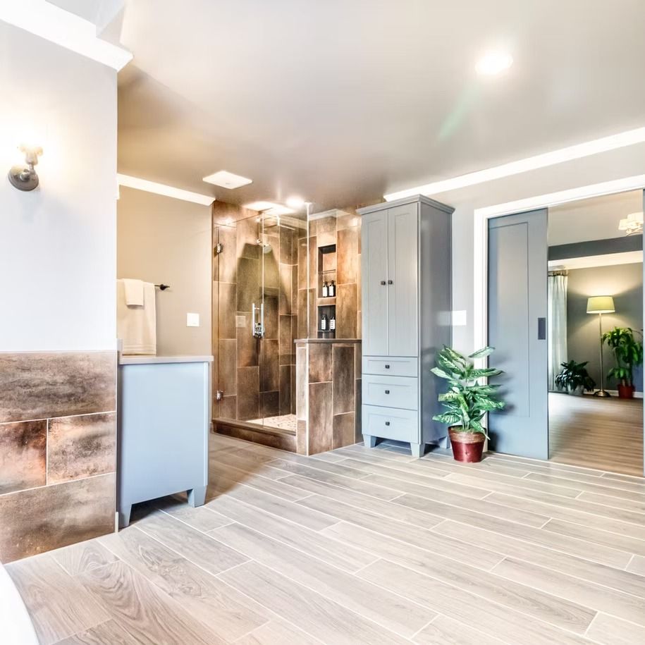Bright modern bathroom with a walk-in shower, gray cabinets, wood-look flooring, and a potted plant