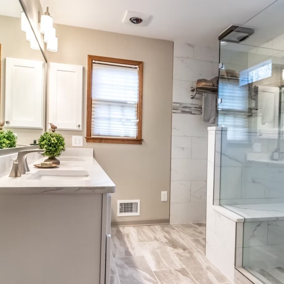 Bright modern bathroom with white vanity, window, tiled shower, and glass enclosure