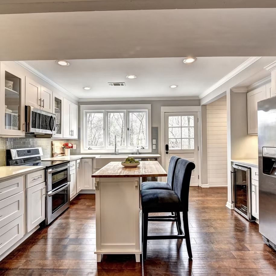 Bright modern kitchen with white cabinets, stainless appliances, island, and large windows.