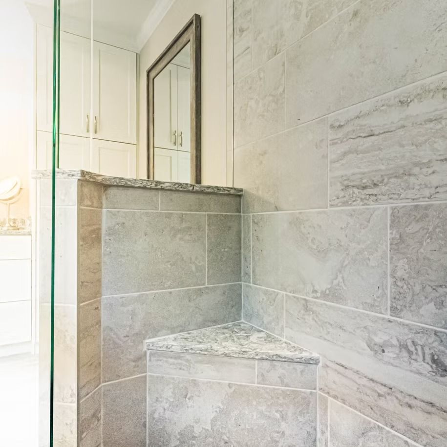 Marble-tiled bathroom shower with glass door, built-in bench, and wall mirror upper ledge