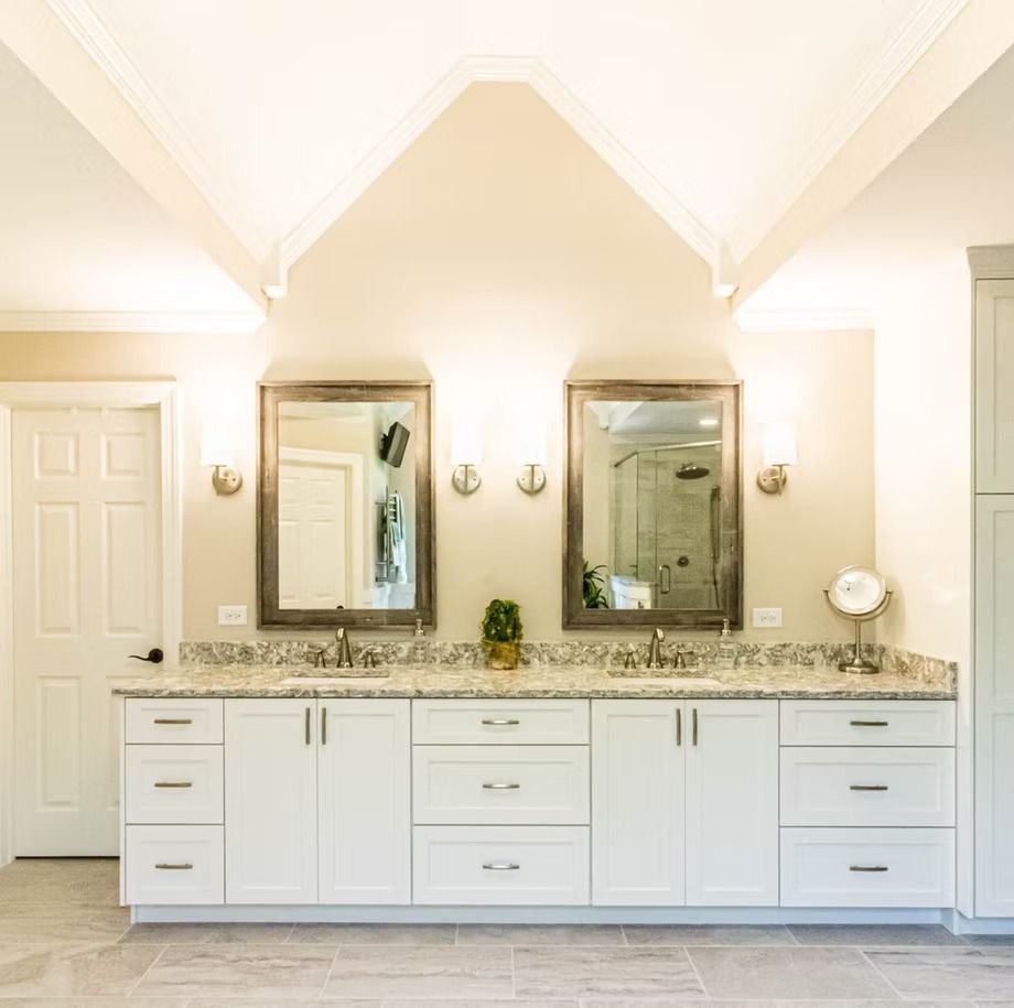 Bright bathroom vanity with two mirrors, white cabinets, granite countertop, and vaulted ceiling
