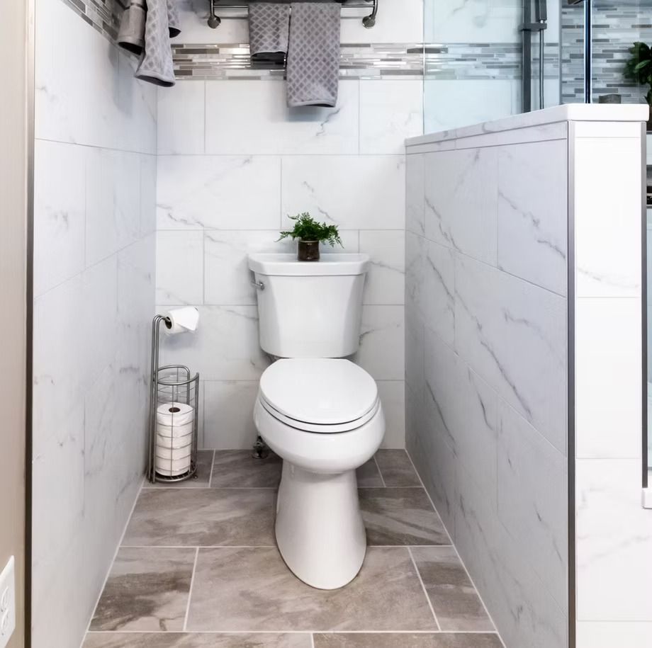 Narrow modern bathroom with a white toilet and marble-patterned walls and floor.