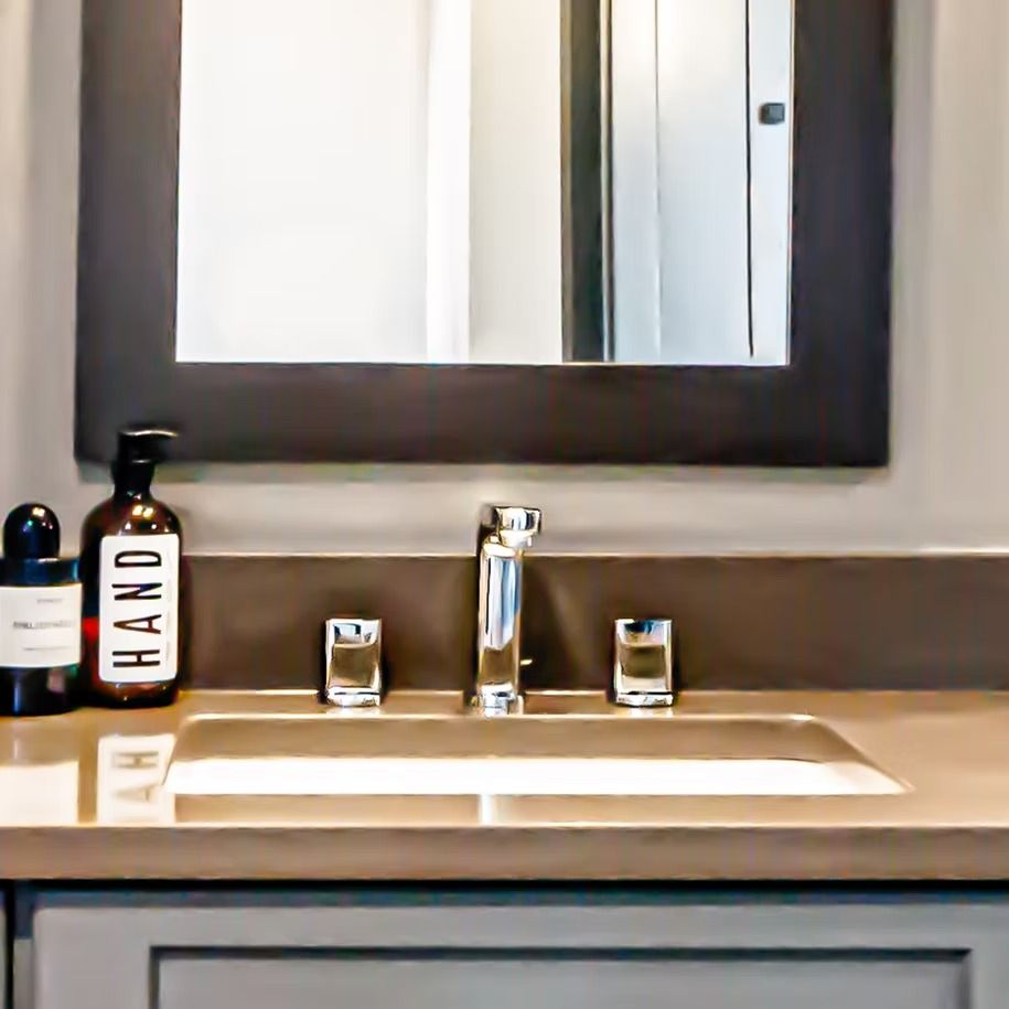 Bathroom sink with mirror, chrome faucet, soap dispensers, and gray countertop cabinets