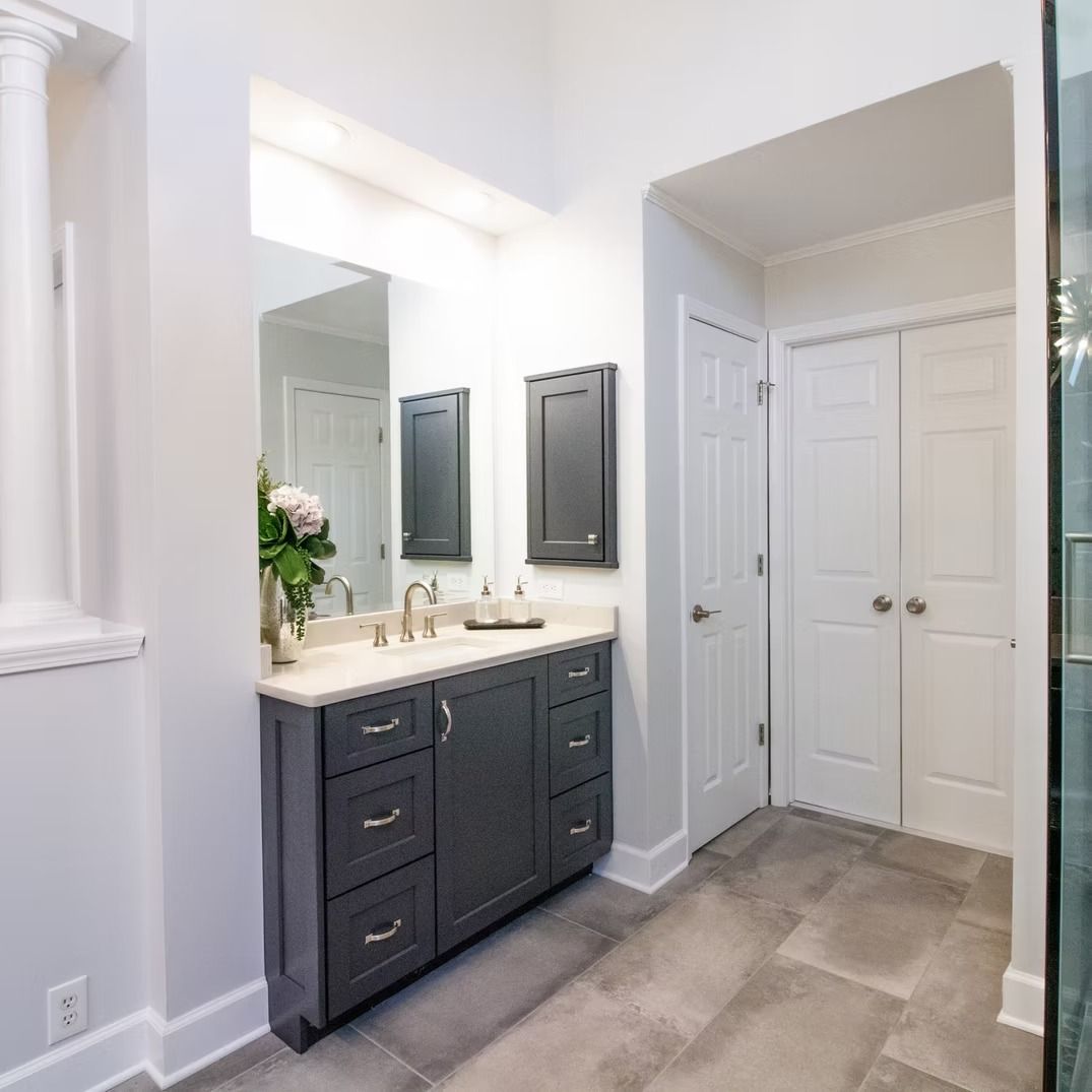 Modern bathroom with dark vanity, large mirror, white walls, and double closet doors