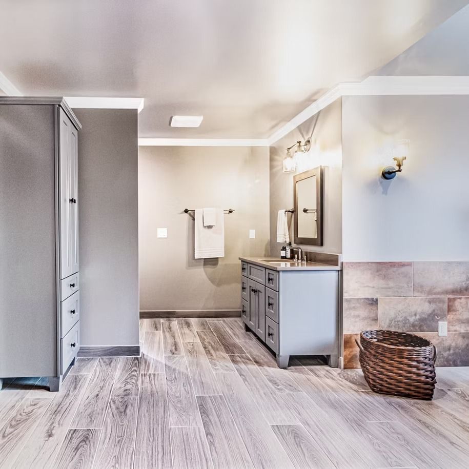 Bright bathroom with double vanity, large mirror, gray tile floor, towel rack, and wicker basket.