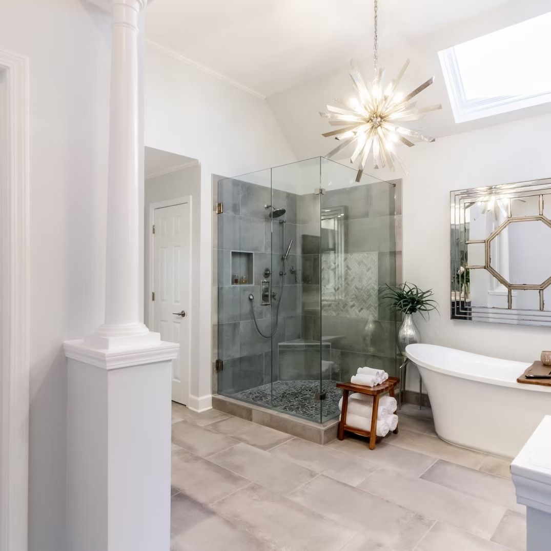 Bright modern bathroom with glass shower, freestanding tub, marble tile, and gold starburst light fixture