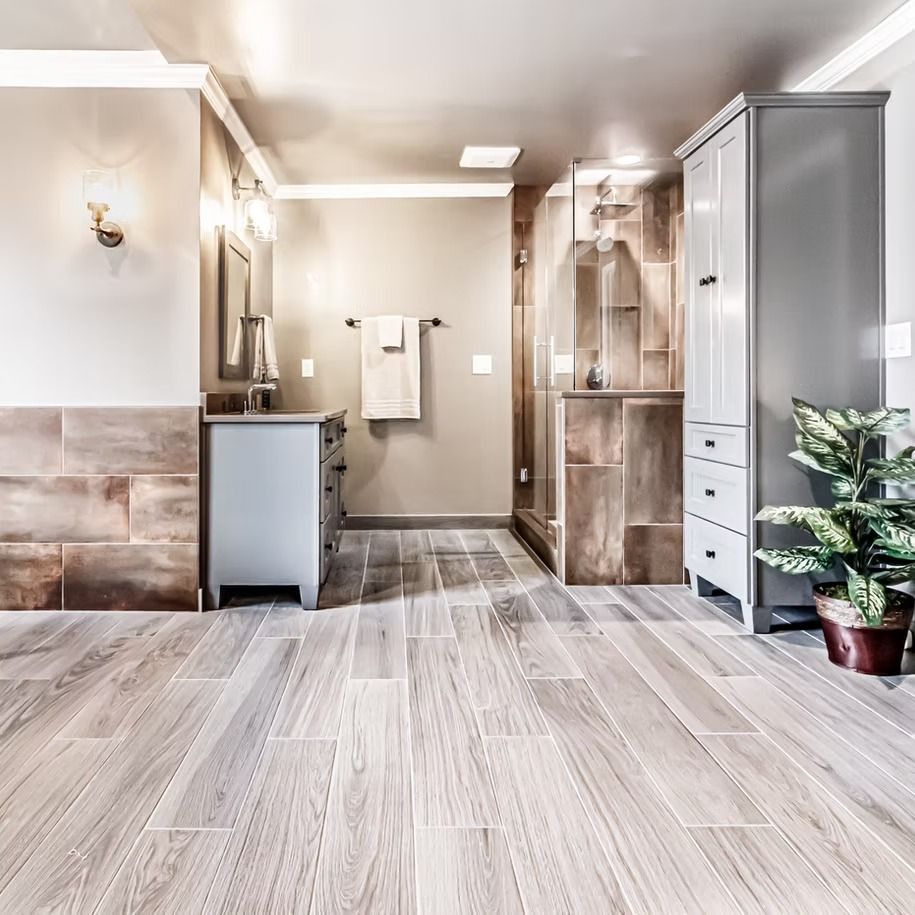 Bright bathroom with gray wood-look tile, vanity, shower, and a potted plant by the wall.