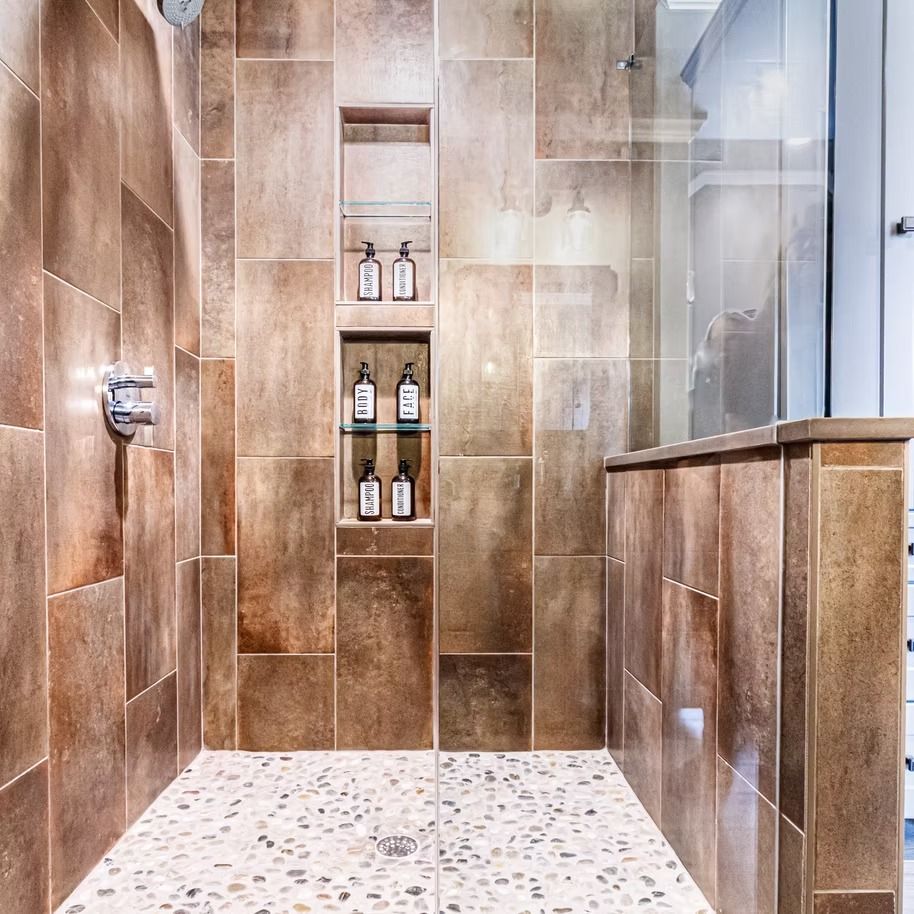 Modern tiled shower with built-in shelves holding soap dispensers and a glass partition