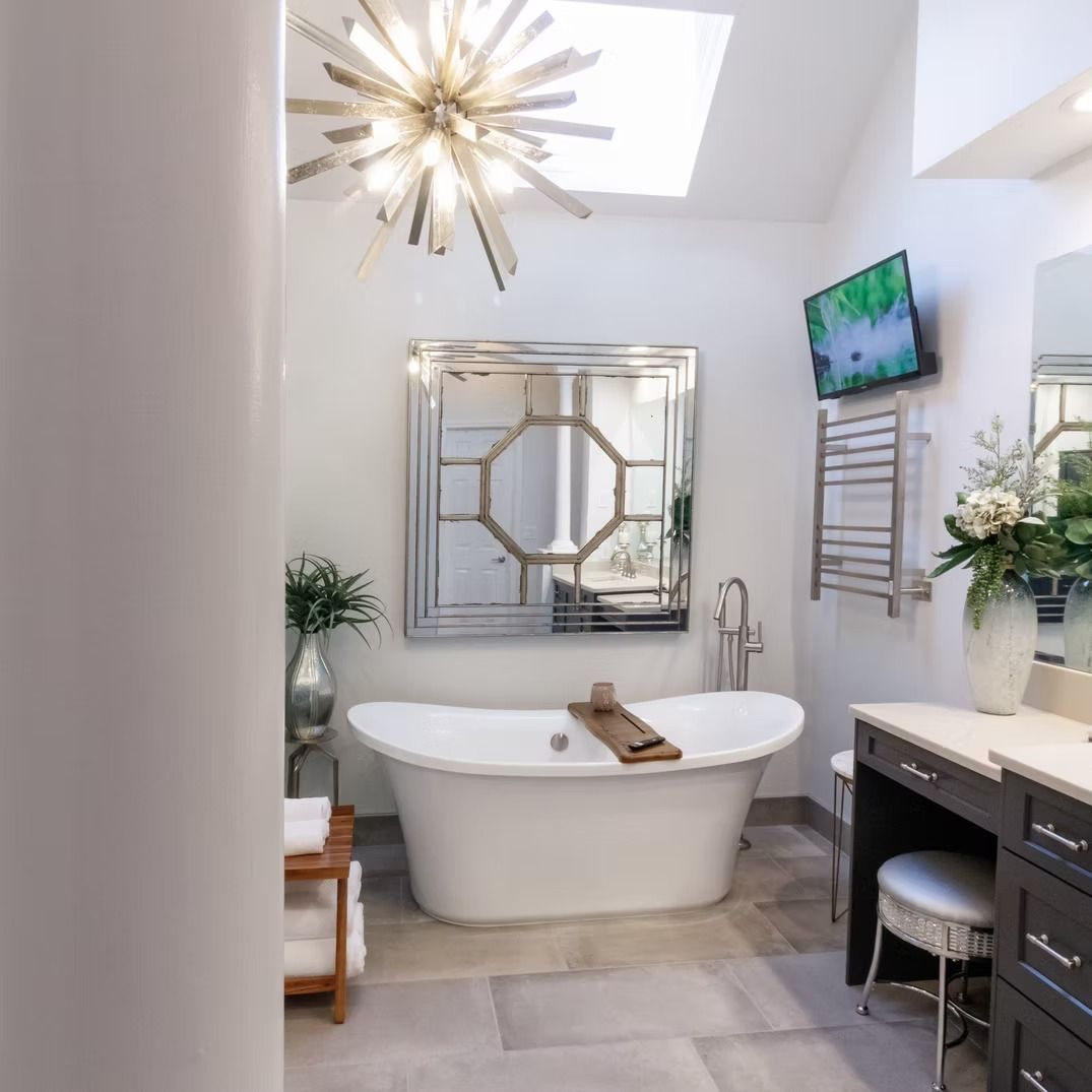 Modern white bathroom with freestanding tub, skylight, gold chandelier, and vanity area