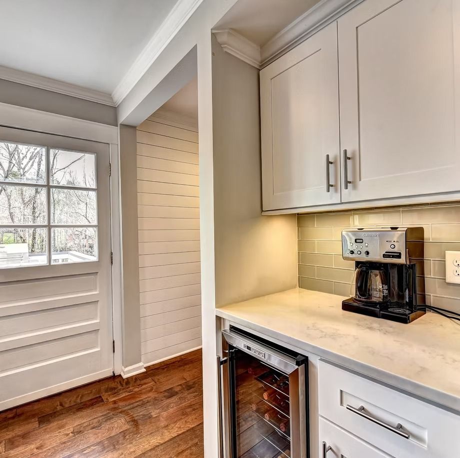 Compact kitchen nook with white cabinets, coffee maker, under-cabinet lighting, and a window by a white door.