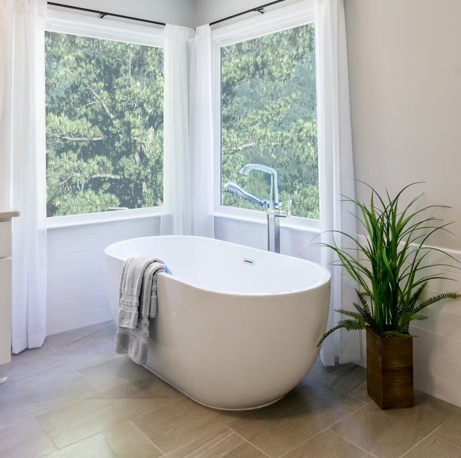Bright modern bathroom with freestanding tub, large windows, and a potted plant