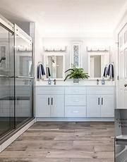 Bright modern bathroom with glass shower, double vanity, mirrors, and wood-look flooring