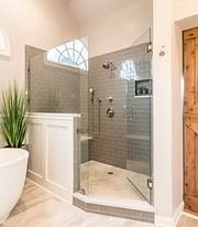 Modern bathroom with glass shower enclosure, white tub, and gray tile walls