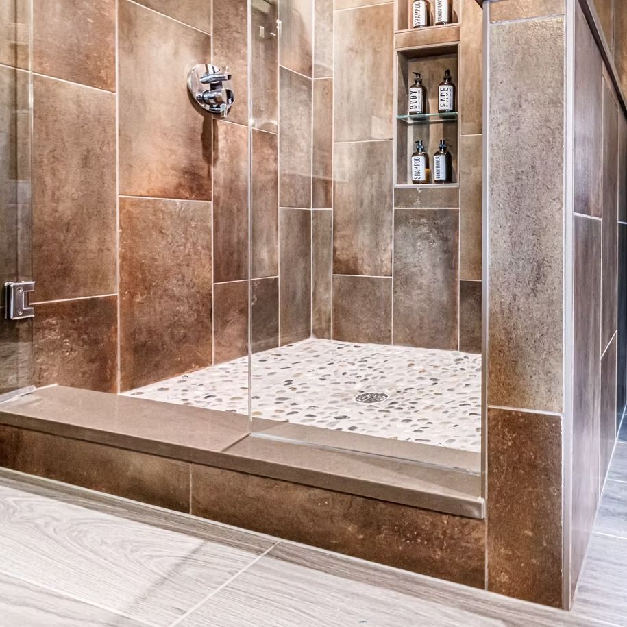 Modern tiled walk-in shower with glass door, built-in shelf, and pebble shower floor