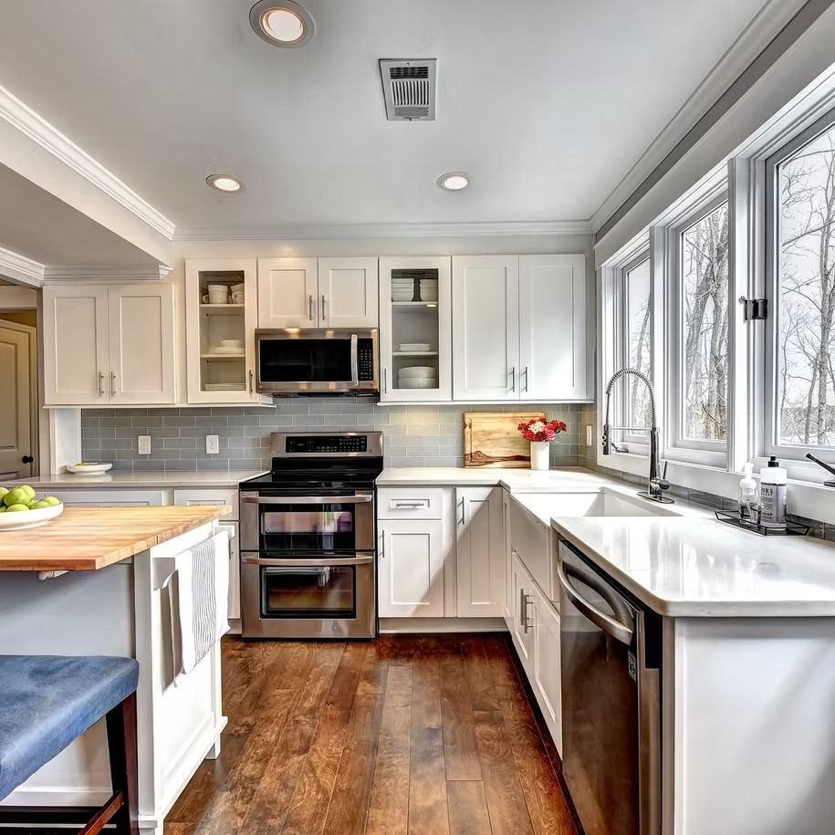 Bright modern kitchen with white cabinets, stainless appliances, wood floor, and large windows over the sink