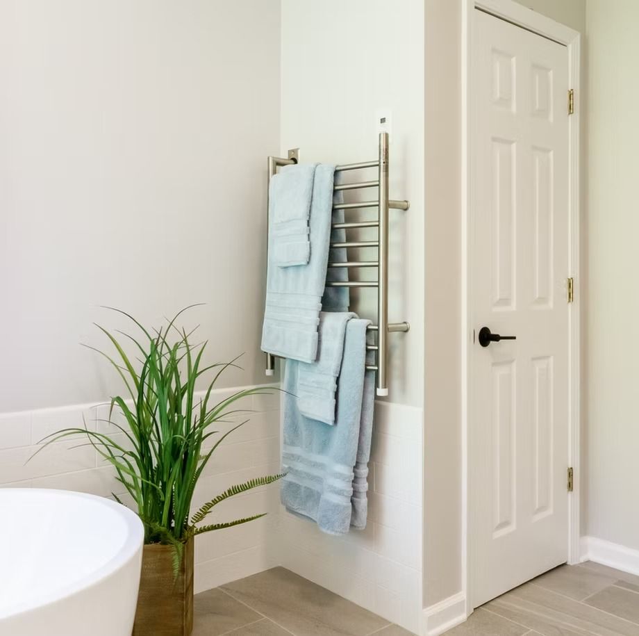 Bathroom corner with towel rack, light blue towels, potted plant, and white door