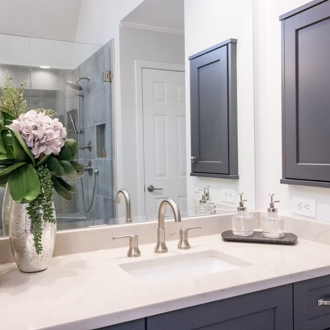 Modern bathroom vanity with white countertop, dark cabinets, mirror, and a vase of flowers