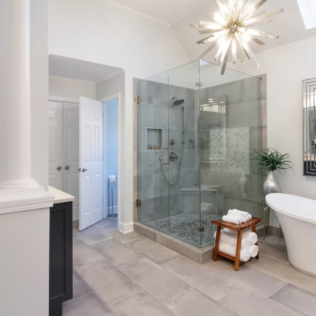Bright modern bathroom with glass shower, gray tile floor, freestanding tub, and starburst ceiling light