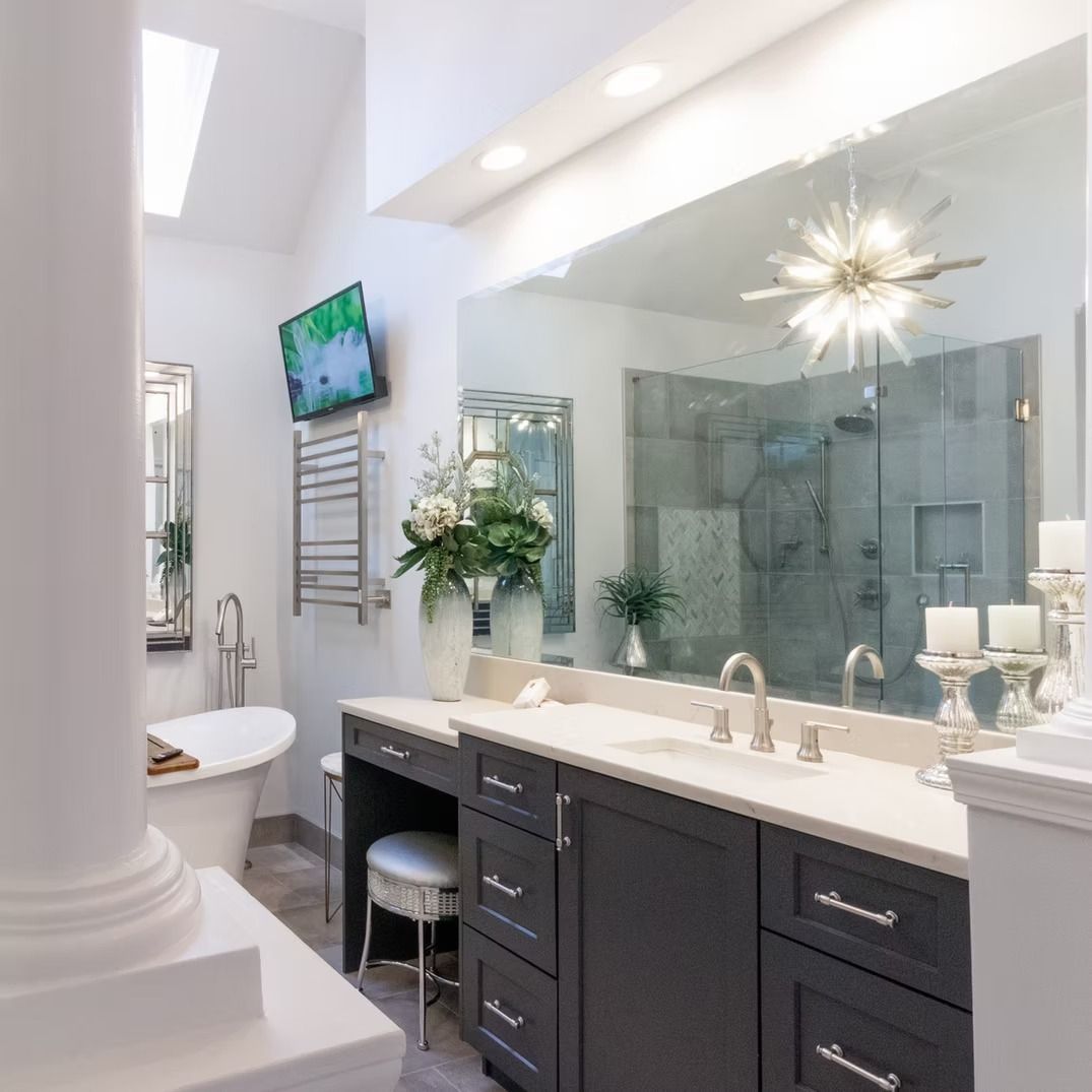 Bright modern bathroom with dark vanity, large mirror, glass shower, and white column in the foreground