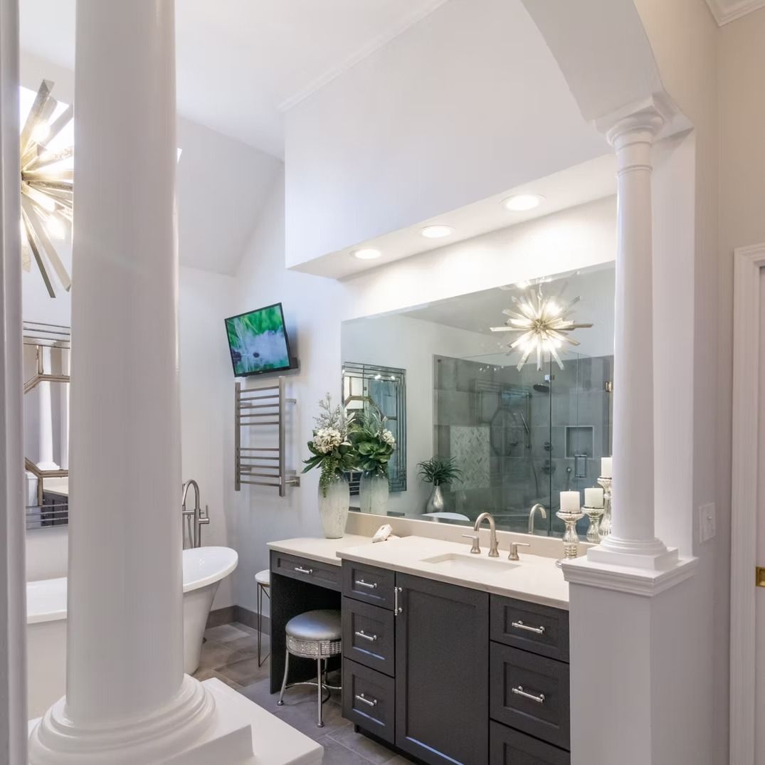 Elegant white bathroom with double vanity, large mirror, wall-mounted TV, and tall columns