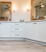 White bathroom vanity with drawers, mirrors, and wall sconces beneath ceiling fans