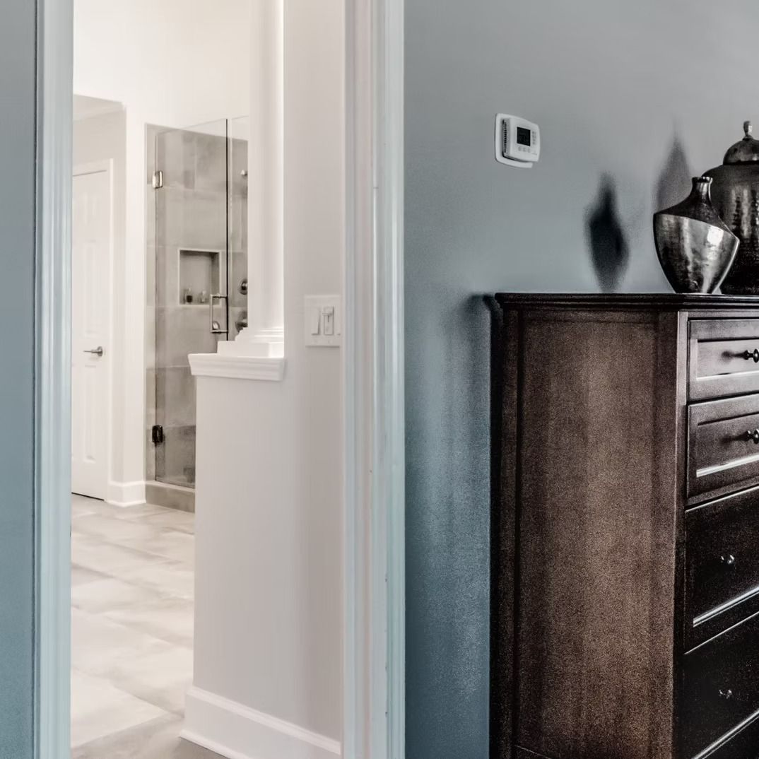 Hallway view into a bright bathroom beside a dark wood dresser in a gray room